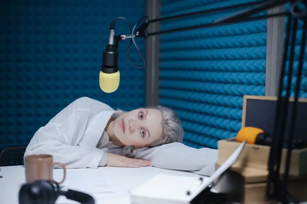 Studio radiowy z mikrofonem i słuchawkami w porannym świetle, anonimowy prowadzący za szybą