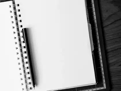 Pusta edytor na laptopie, notatnik z zapisanymi tytułami i długopis