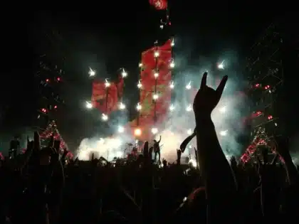Anonimowy tłum przed rozświetloną sceną festiwalową, sylwetki i podniesione ręce