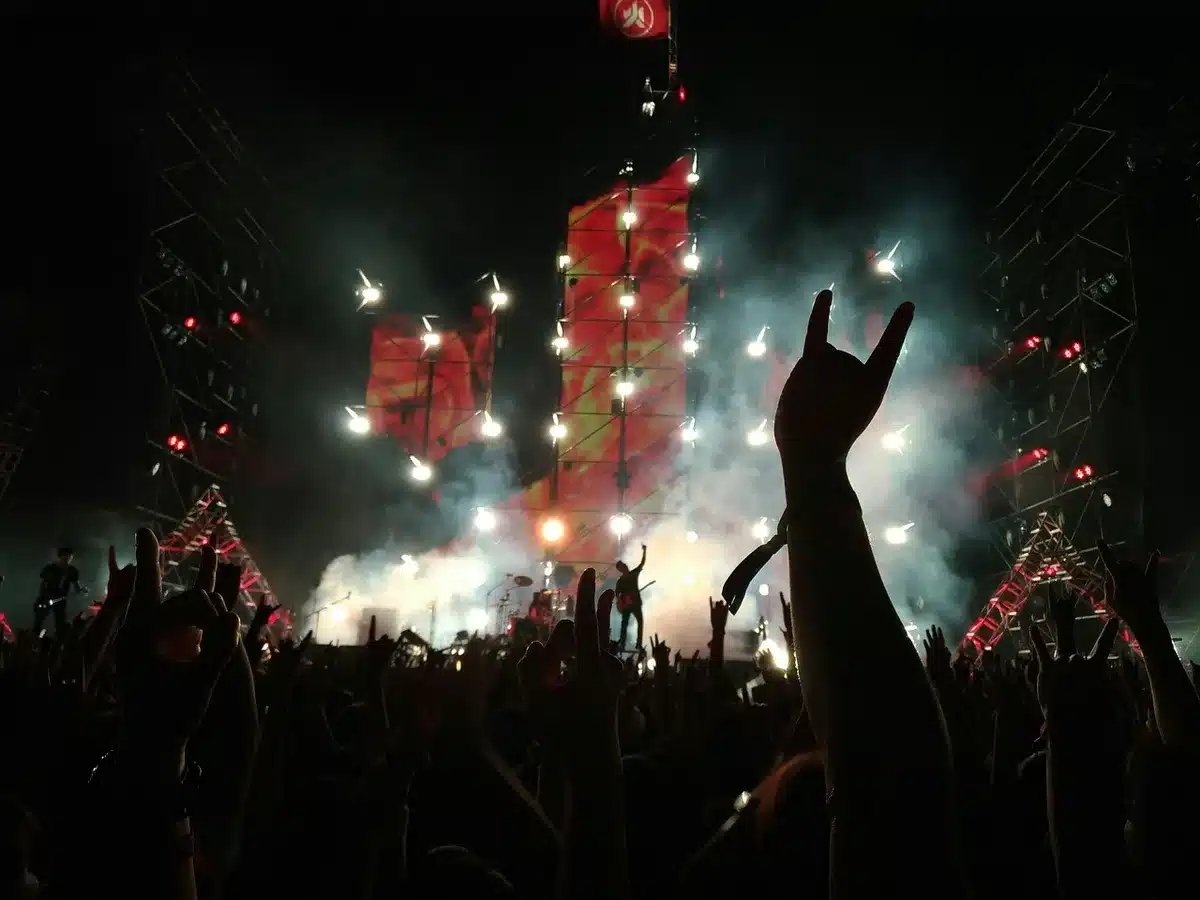 Anonimowy tłum przed rozświetloną sceną festiwalową, sylwetki i podniesione ręce