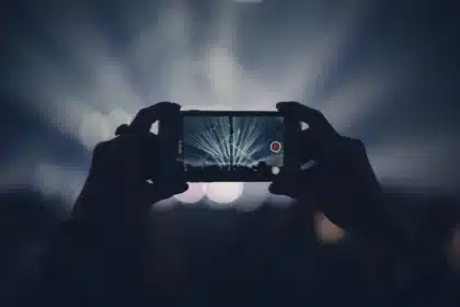 Sylwetki publiczności z podniesionymi rękami przed oświetloną sceną na stadionie